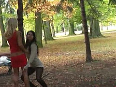Sassy girls are posing on cam standing along the tree in a public park